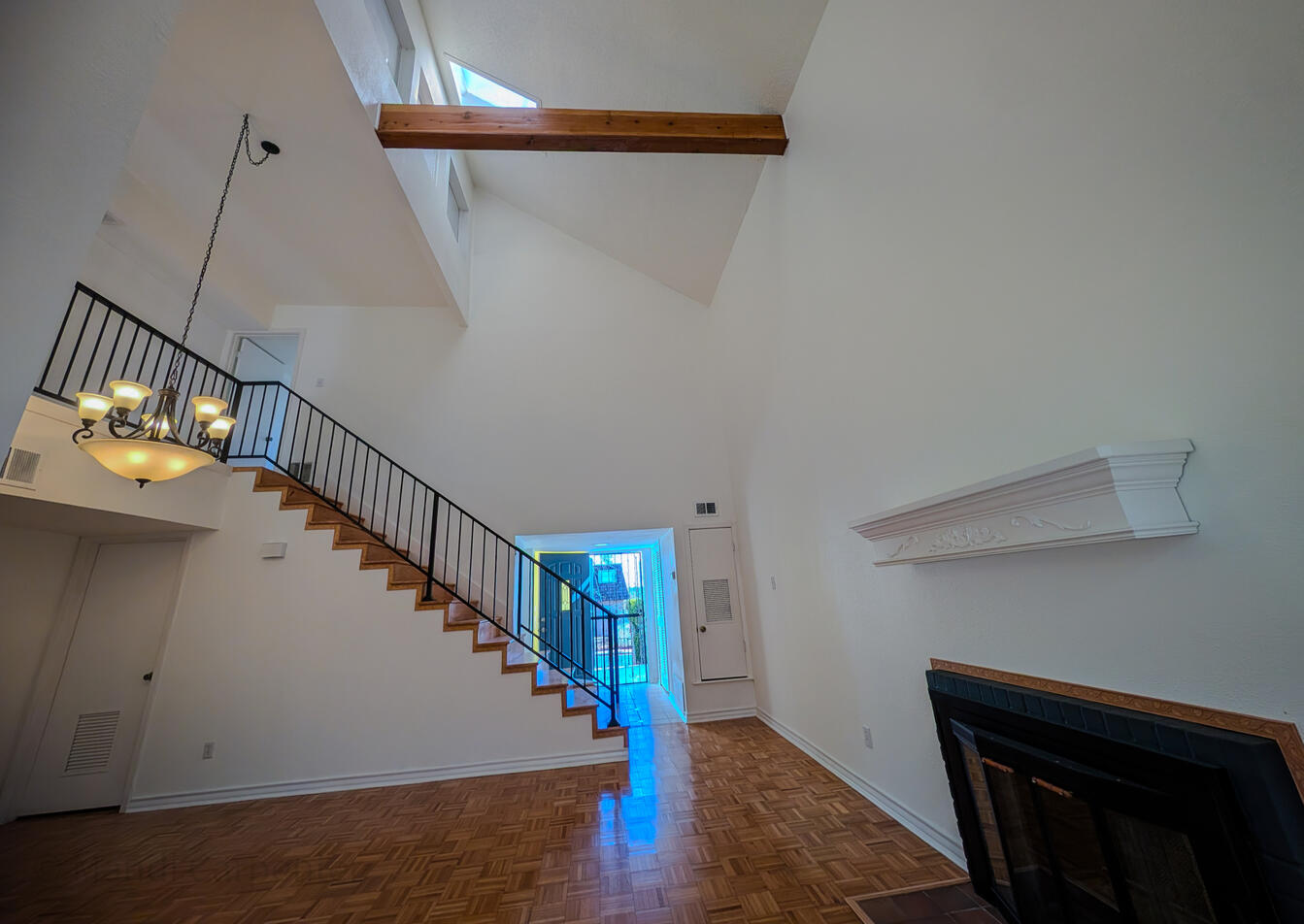 Main Room as seen from the second living area, the fireplace can be seen, along with white walls, golden natural wood floors matching the oak faced staircase and both stair and fireplace are bordered with an Ivy leaf trim
