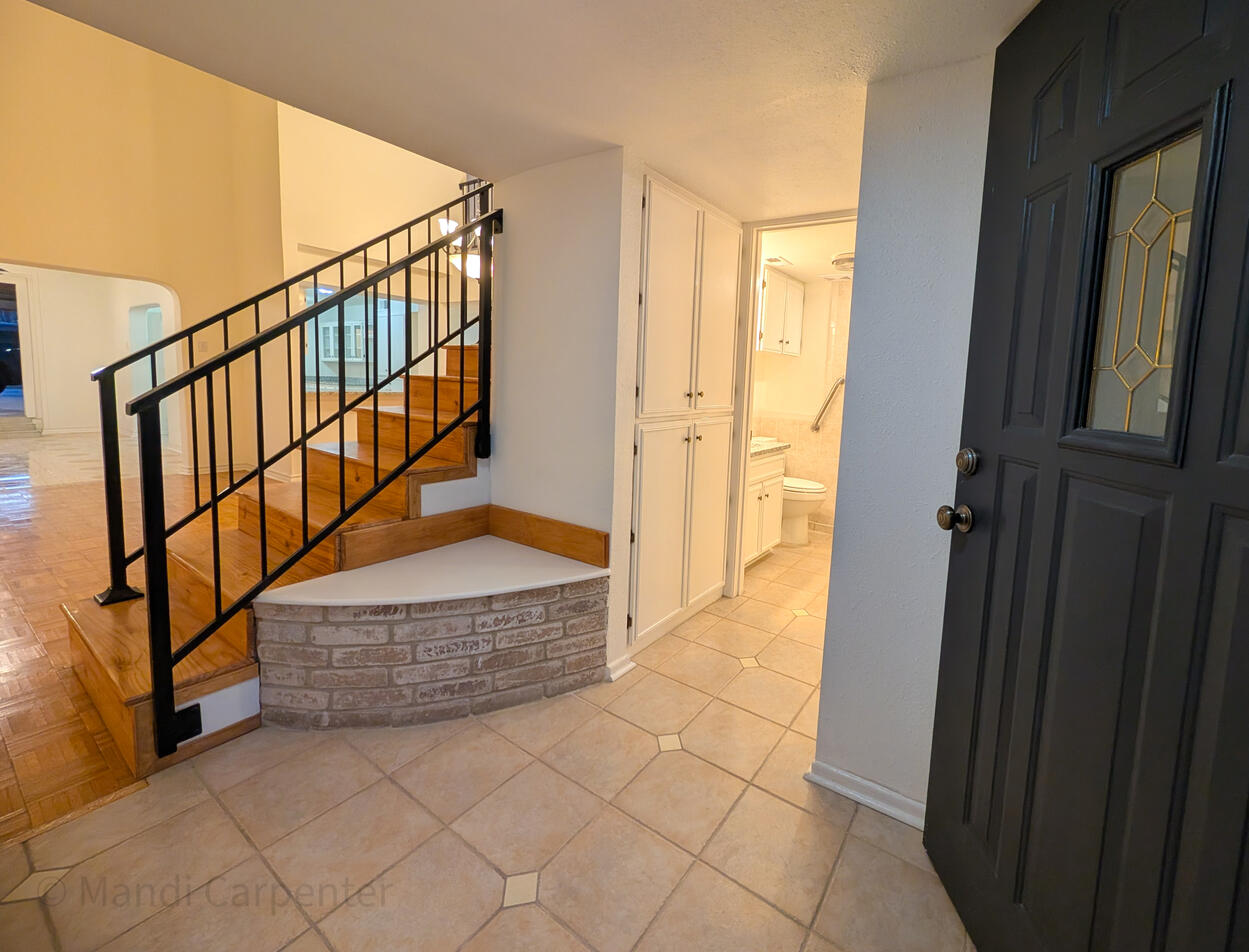 A solid dark painted door with a welcoming glass panel are open leading you into the tiled Foyer with a vintage brick seat with hidden storage to take off your shoes and then you can see Large storage cabinets and entry to the lower bed and bath area